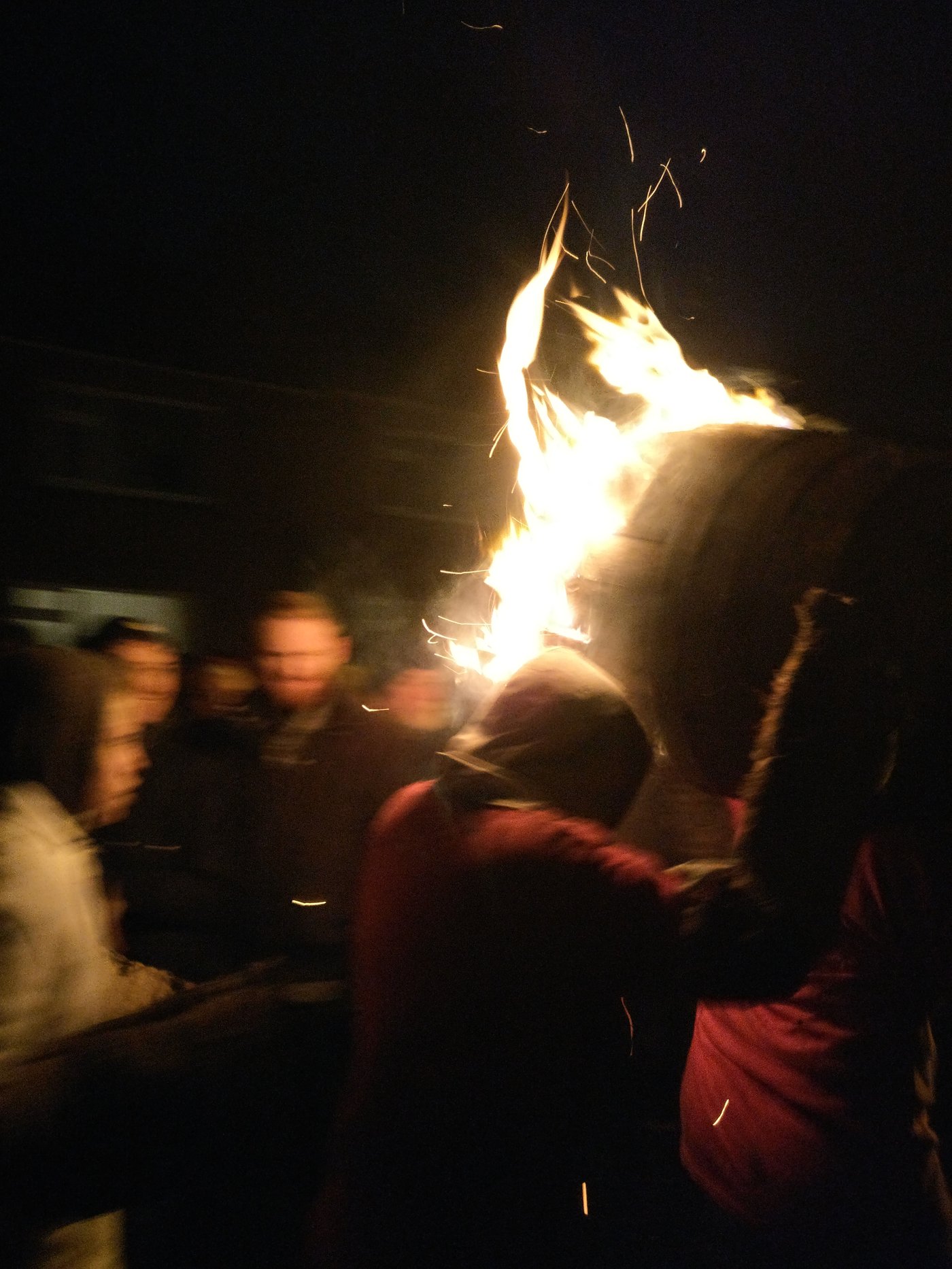 A man runs through a crowd with a burning barrel in Ottery St Mary