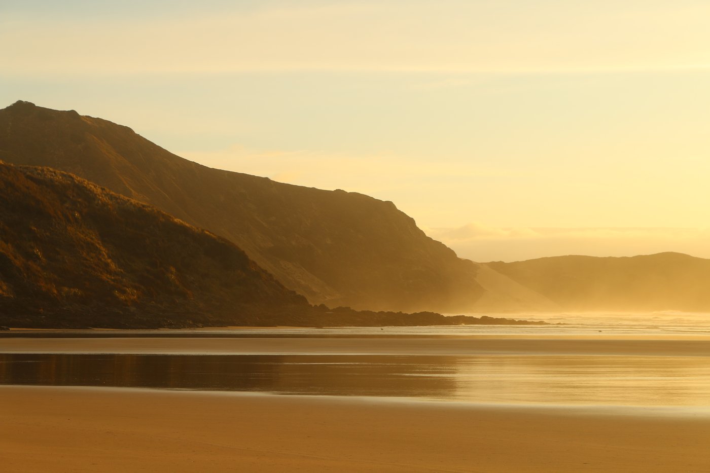 The golden hour illuminates the headland on Te Werahi beach