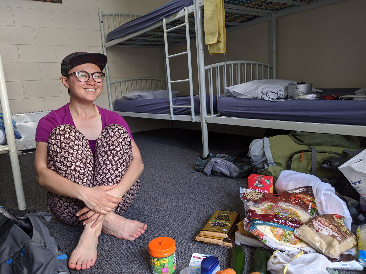 Rose sits on the floor of our hostel dorm room, some of our grocery shopping is visible beside her.