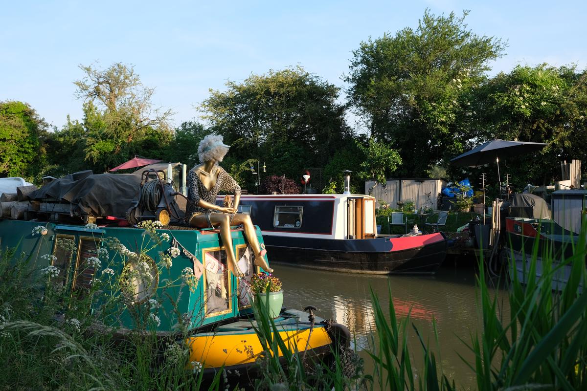 A mannequin sits on a narrowboat, looking out over the water.