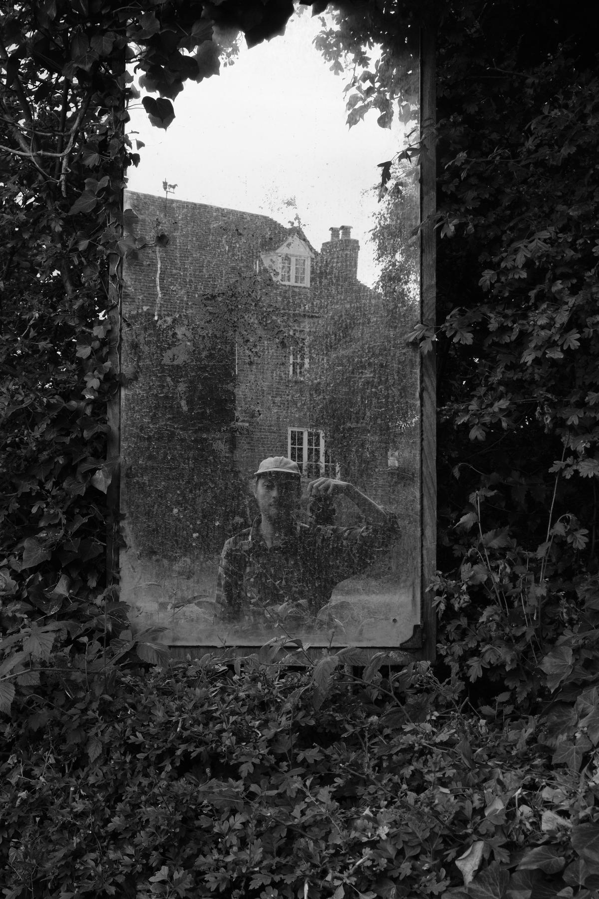 A self-portrait in a tall mirror set into a country hedge
