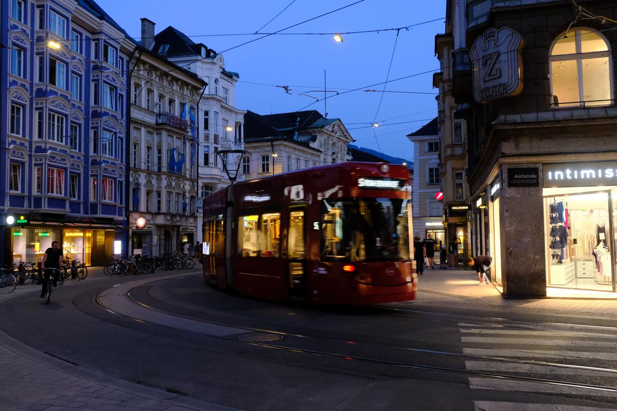 A cyclist and a tram take a corner while a woman bends to tie her shoe. Innsbruck, Austria