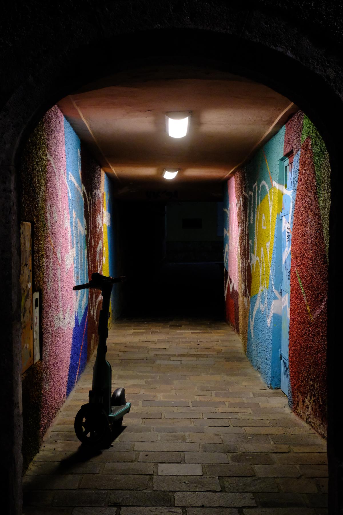 An electric scooter sits in shadow in a brightly painted tunnel at night. Innsbruck, Austria