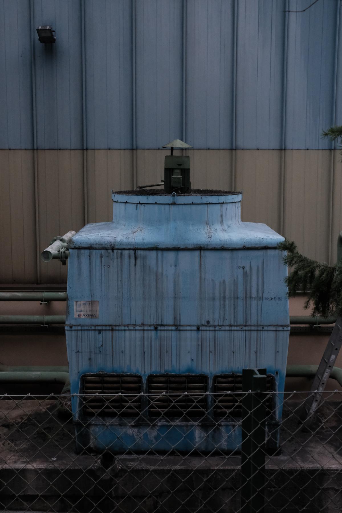 A soviet era generator sits between a fence and the two tone exterior of a factory near Idrija, Slovenia