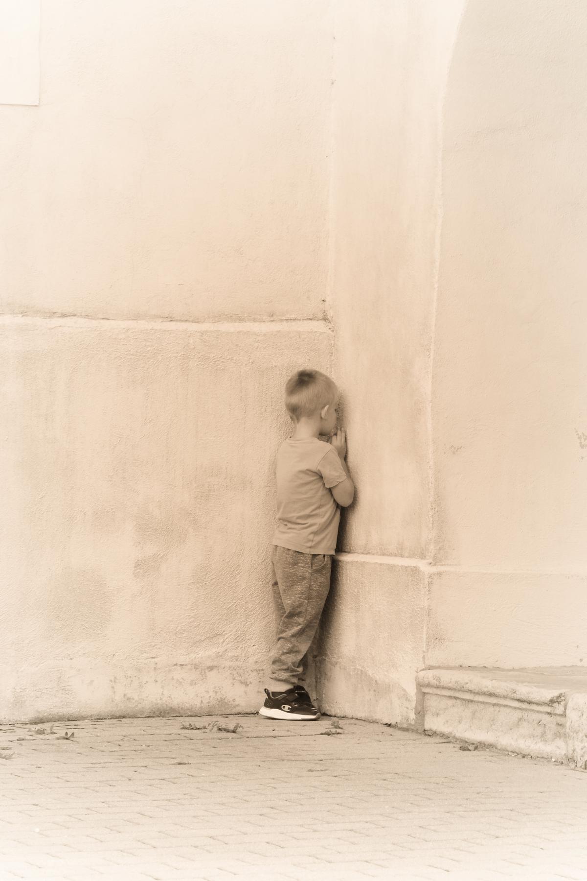 A child presses himself into a corner while playing hide and seek with his grandfather, southern Slovenia