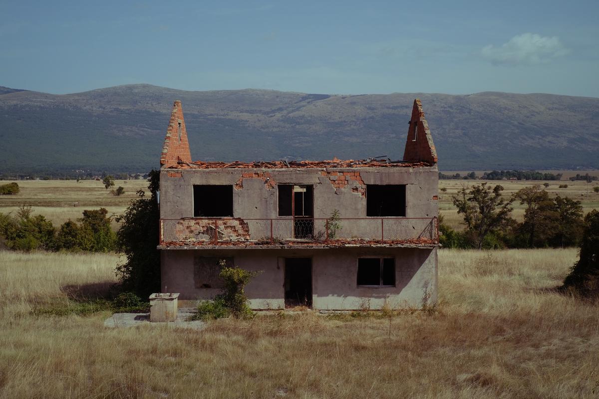 An abandoned house with a collapsed roof, seen from a highway in rural Bosnia