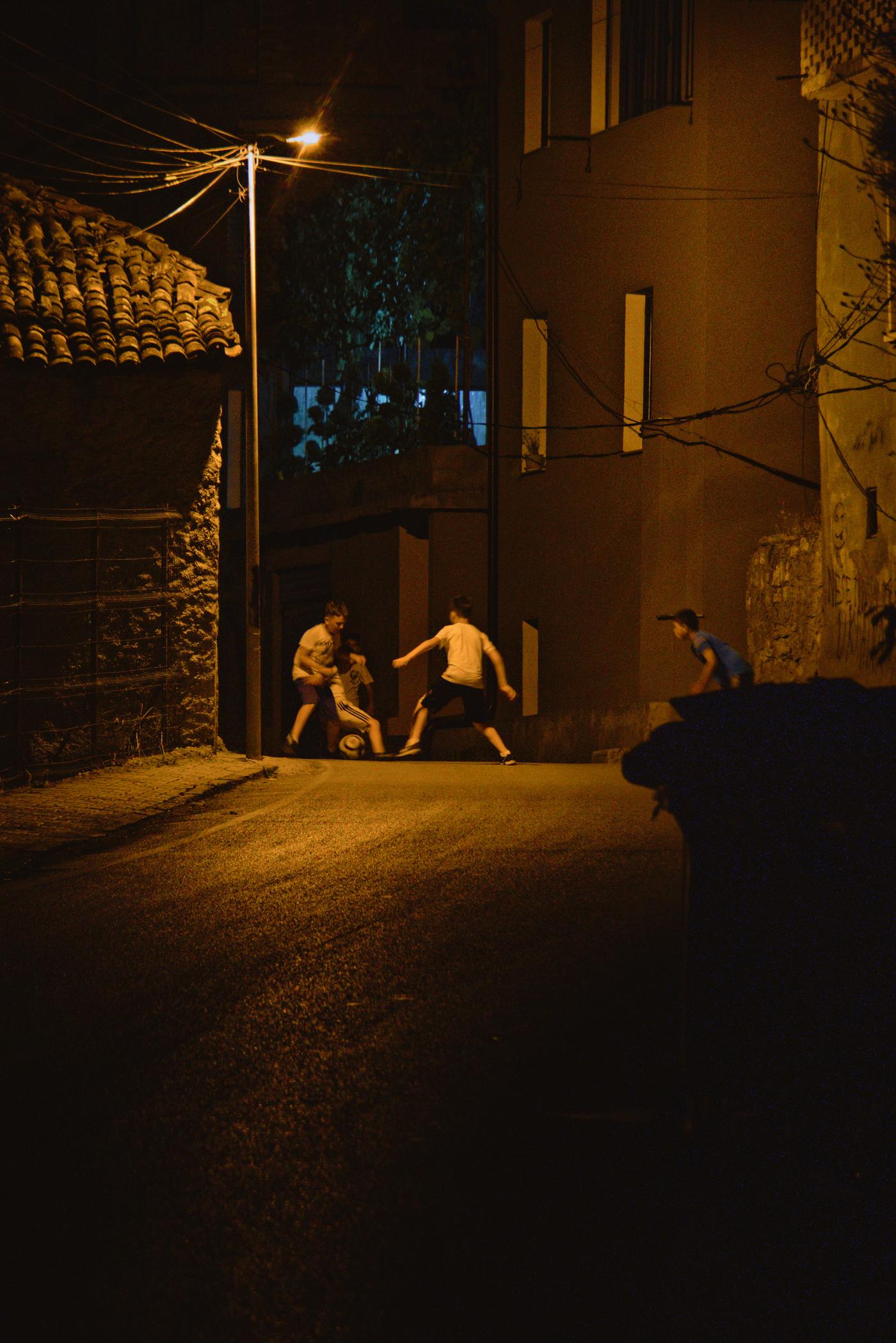 Four boys play football in the street late into the night. Peshkopi, Albania