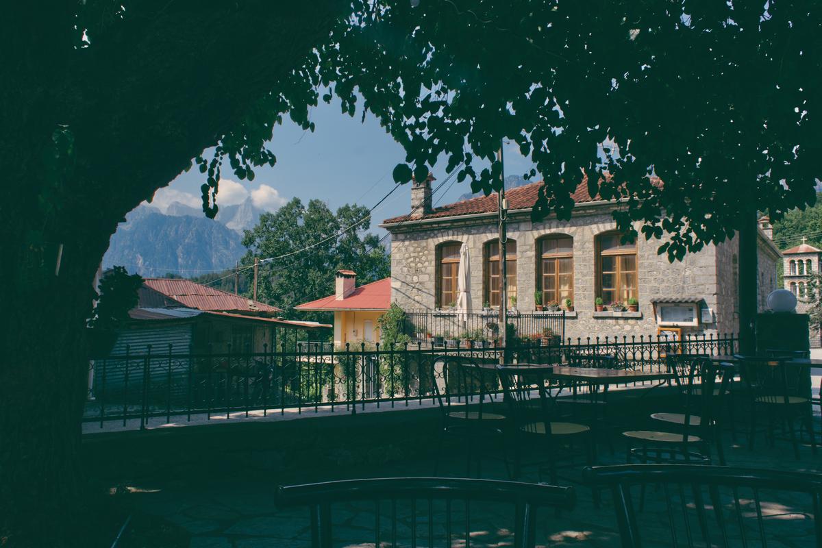 An enclosed square containing a great big tree, a statue, and an eclectic mix of tables and chairs in Eleuthero, Greece.