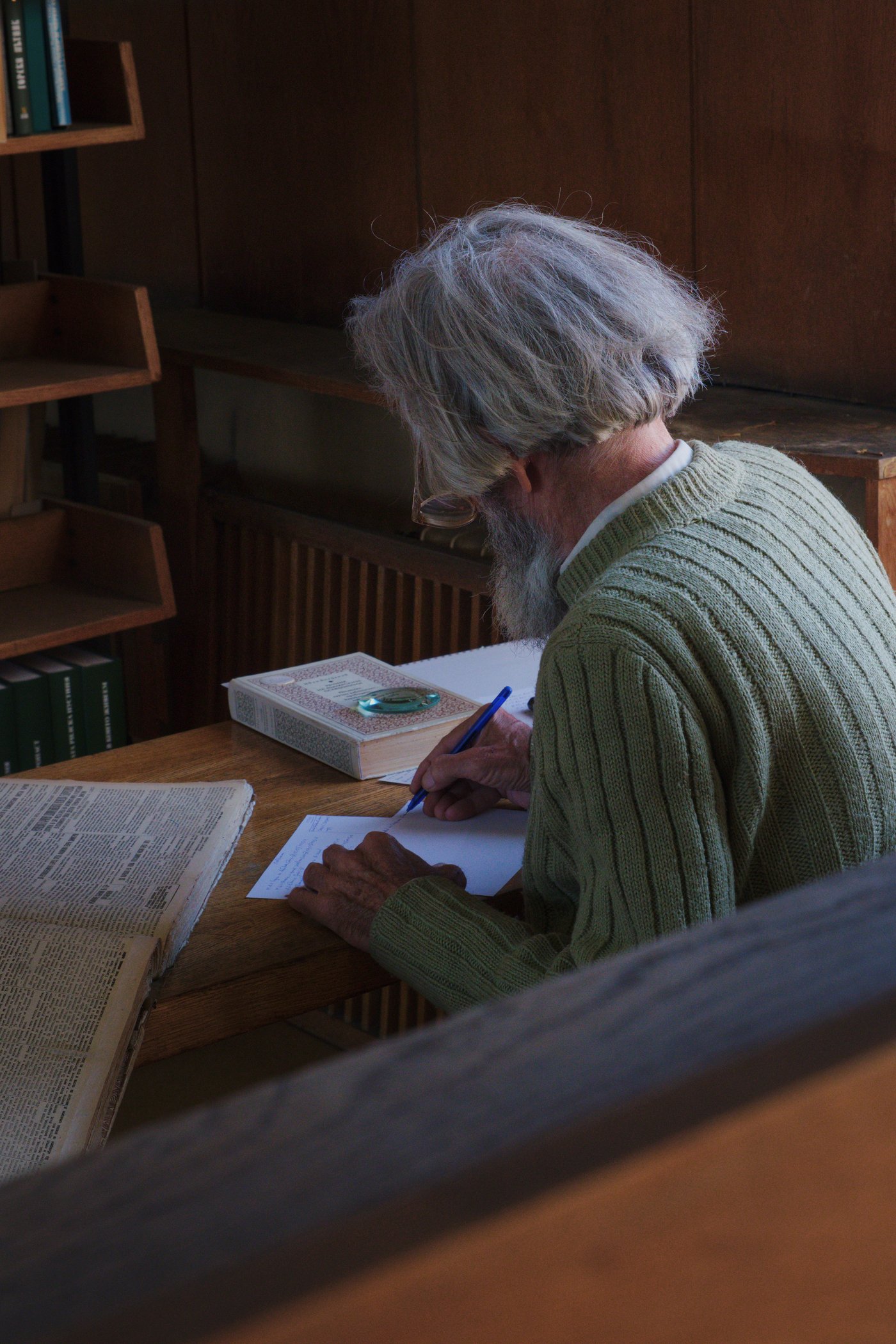 A man sits at a desk, writing, a large volume open in front of him. The Ivan Vazov National Library. Plovdiv, Bulgaria