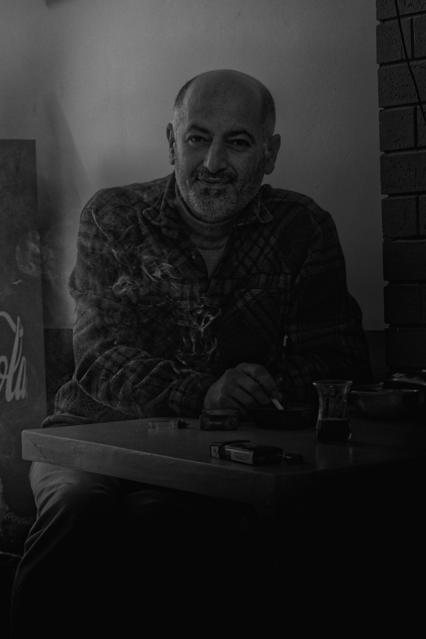 Nihat sits at a table in his cafe, smoking a cigarette, looking at me, unsure if/how to pose for his photo. Istanbul, Turkey