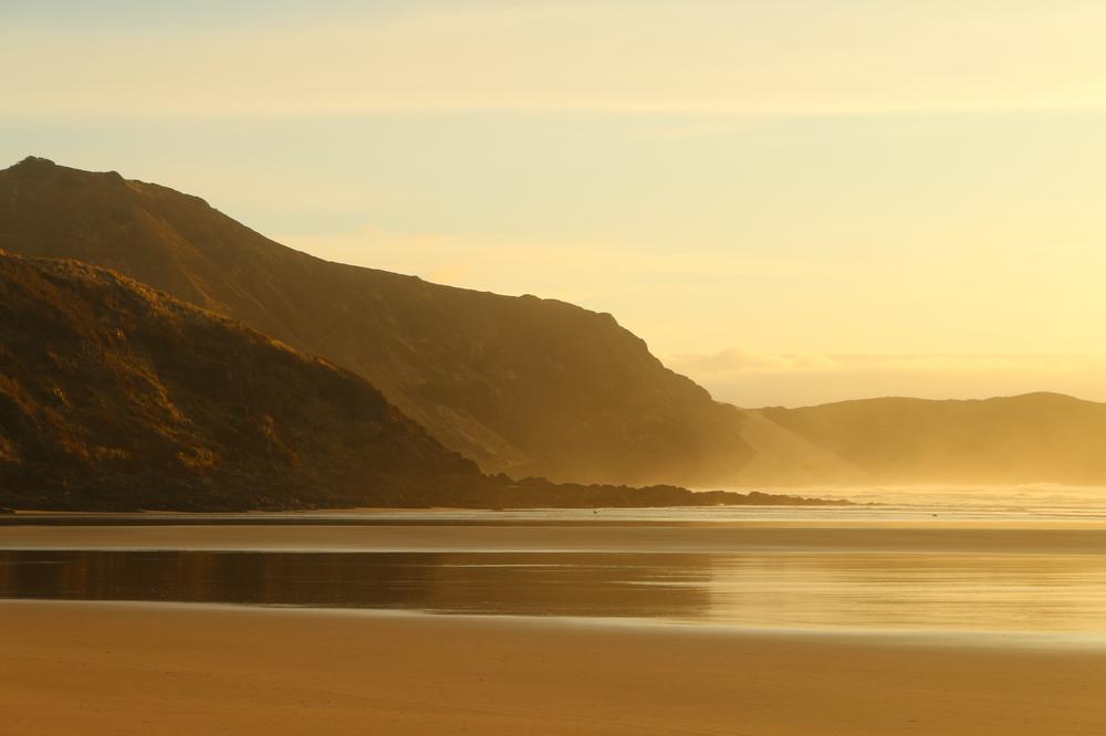 The golden hour illuminates the headland on Te Werahi beach.
