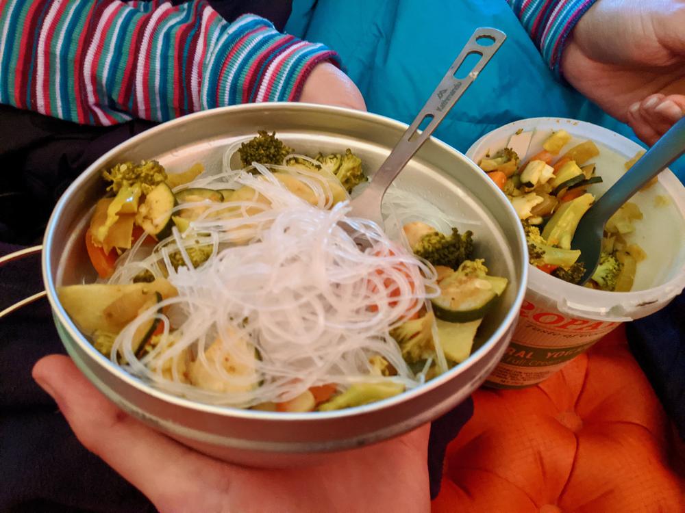 A meal of rice noodles and veggies in the shelter of the tent.