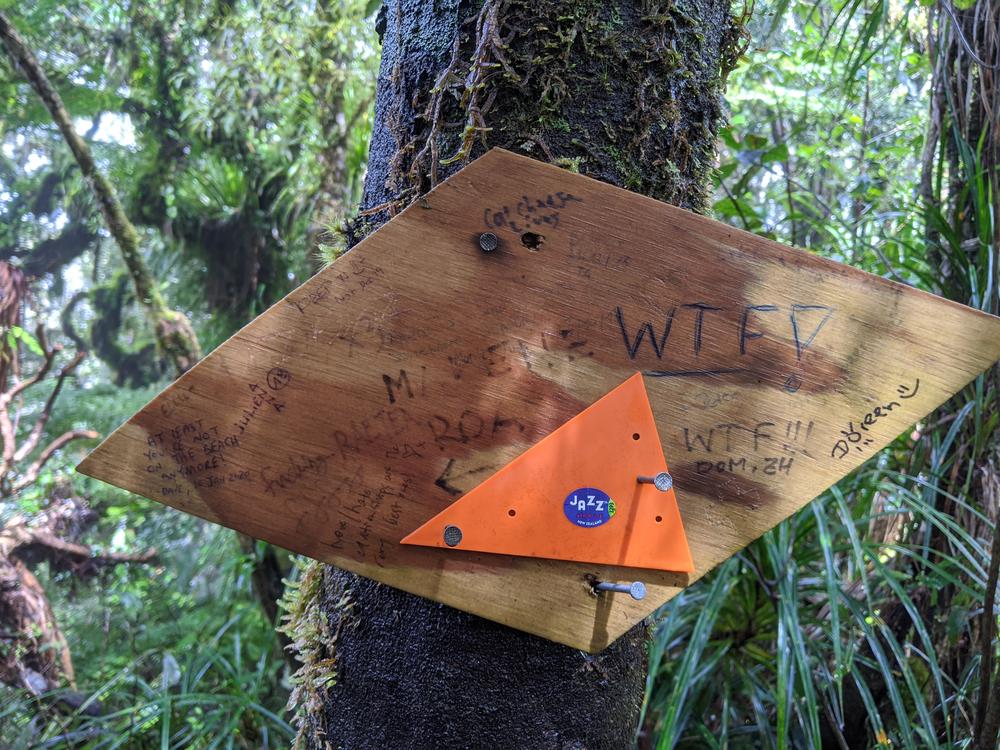 An orange trail marker adorned with messages from previous hikers.