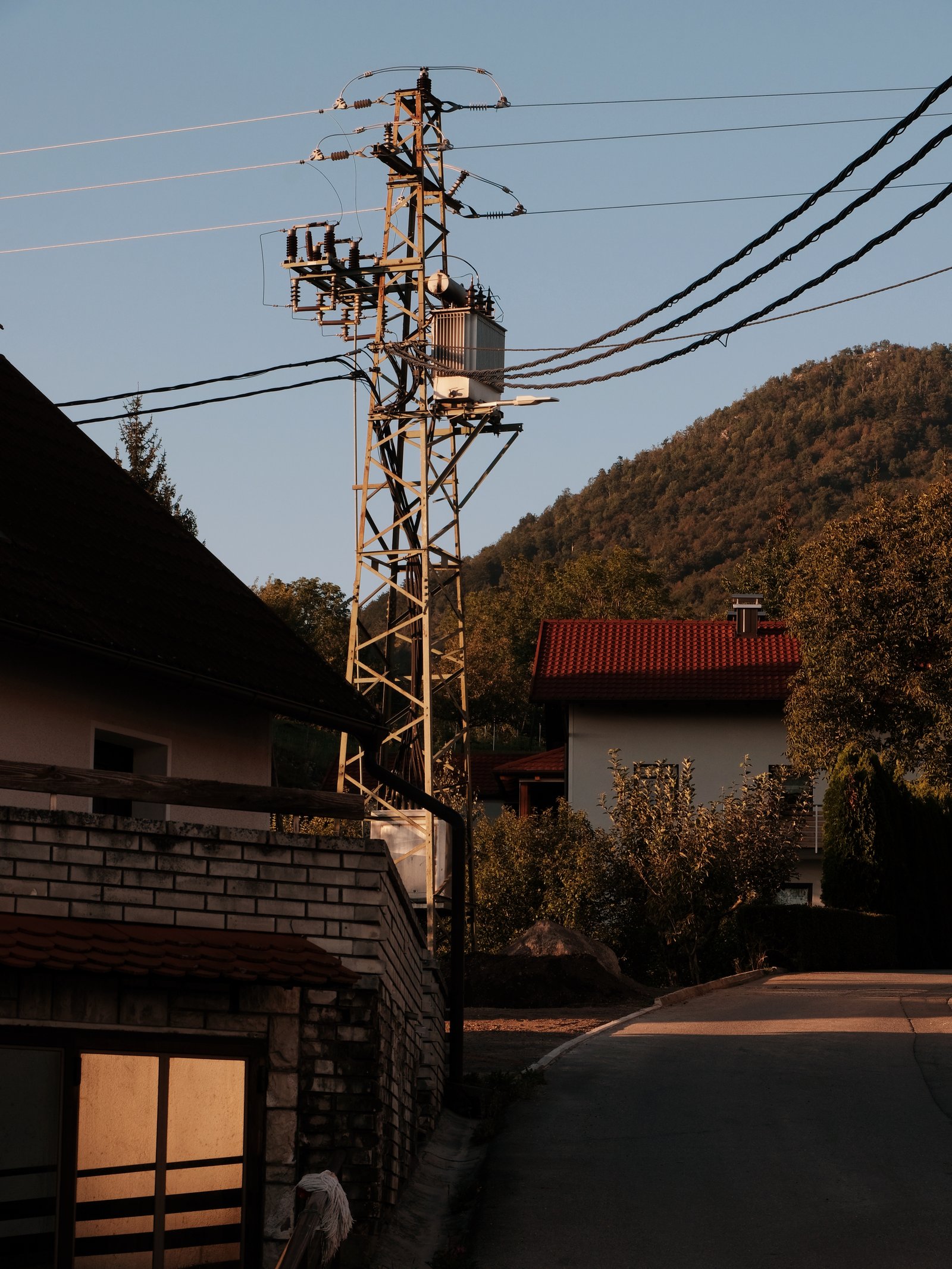 A dark sweeping driveway, sharp brickwork above a garage in shadow save for the sunglow reflected off a one way window. Studeno, Postojna, Slovenia.