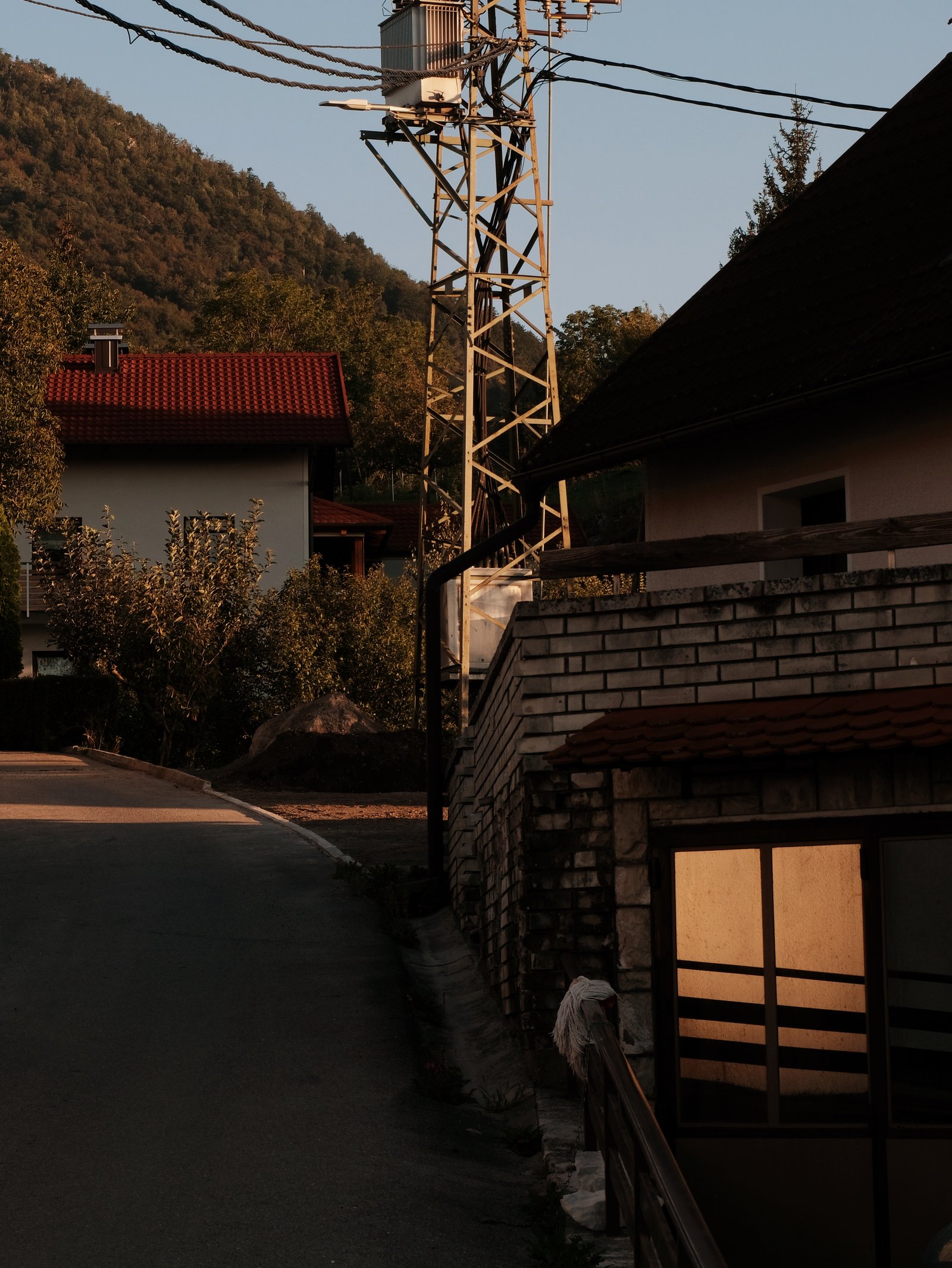 A dark sweeping driveway, sharp brickwork above a garage in shadow save for the sunglow reflected off a one way window. Studeno, Postojna, Slovenia.