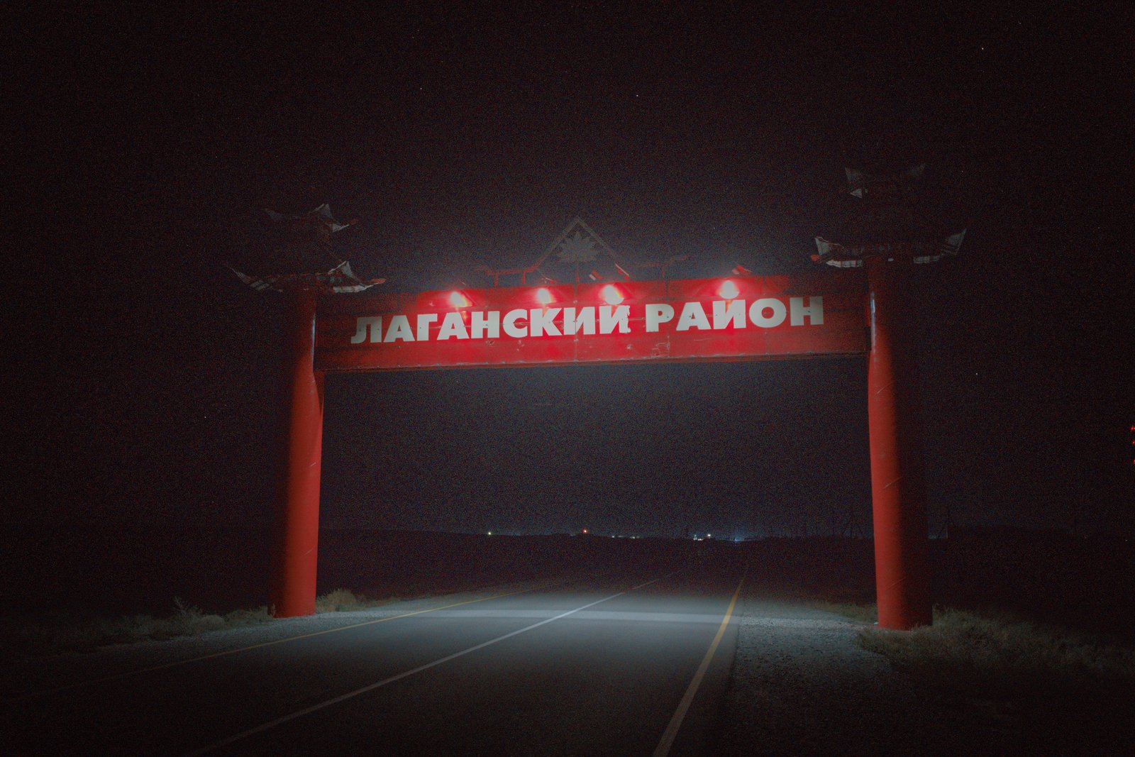 A brightly lit sign over the road reads ЛАГАНСКИЙ РАЙОН (Lagansky District). The style of the sign reflects the Mongolian heritage and Buddhist faith of the people of Kalmykia. Russia